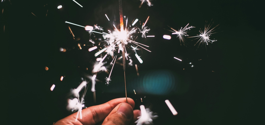 Een persoon houdt een sterretje vast, met een sprankelende gloed in de hand tijdens een feestelijke gelegenheid.