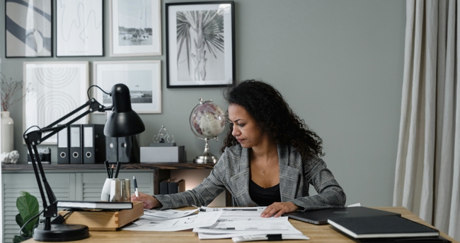 Een vrouw is aan het werk aan haar bureau in haar thuiskantoor, met een laptop en notities voor zich.