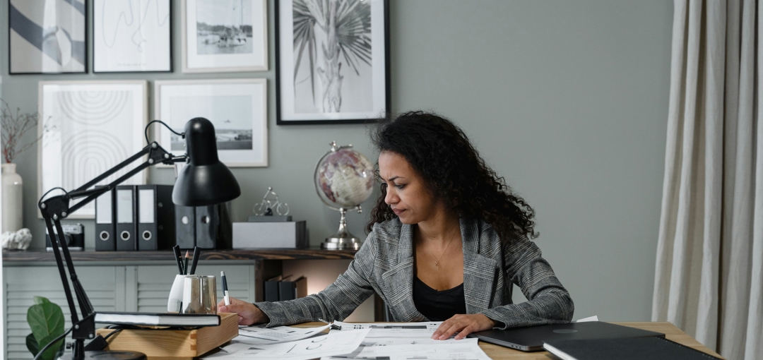 Een vrouw is aan het werk aan haar bureau in haar thuiskantoor, met een laptop en notities voor zich.