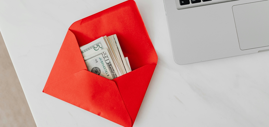 Een laptop op tafel met een envelop vol geld